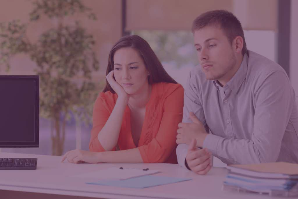 A man and a woman are sitting at a desk in front of a computer.