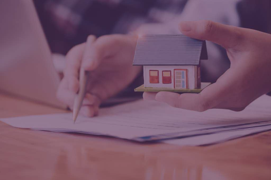 A person is holding a model house in their hand while signing a document.