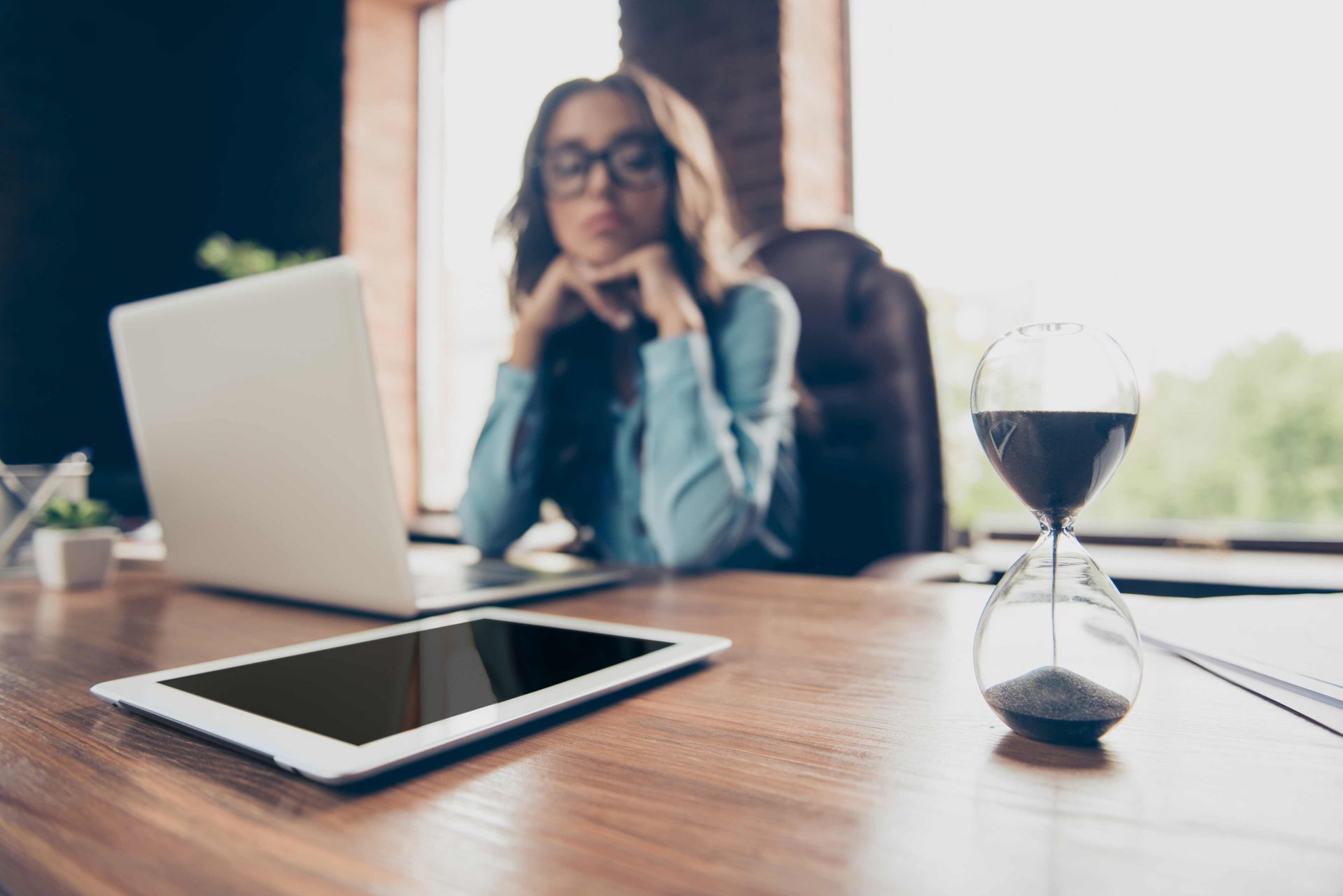 A woman looking at the time via an hourglass on her desk