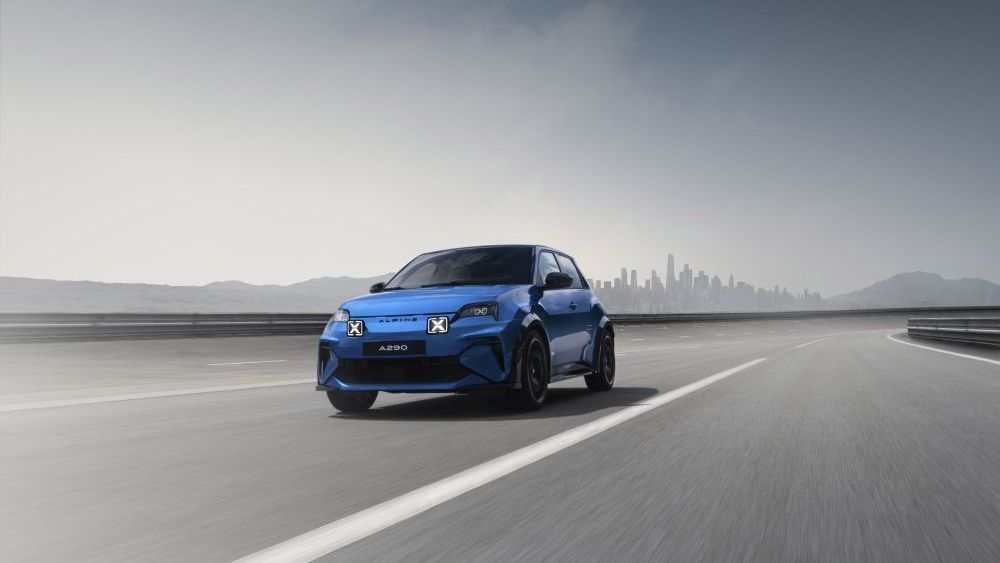 Een blauwe Alpine A290 rijdt over een weg met in de verte een stad op de achtergrond