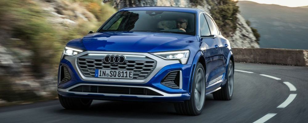 Een felblauwe Audi SQ8 e-tron  quattro rijdt in de bergen door een scherpe bocht