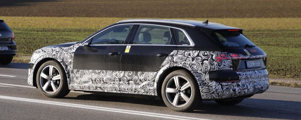 Een gecamoufleerde zwarte Audi e-tron rijdt over een 4-baans weg langs landerijen