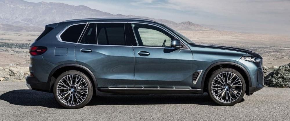 Een blauw metallic BMW X5 staat geparkeerd in een ruwe omgeving