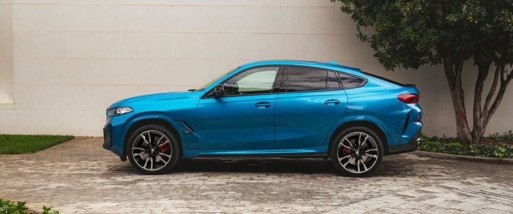 Een blauwe BMW X6 staat geparkeerd bij een muur en een boom