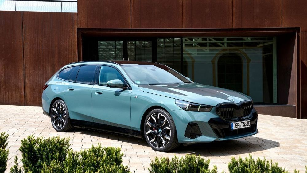 Een lichtblauwe BMW i5 eDrive40 Touring staat voor een gebouw