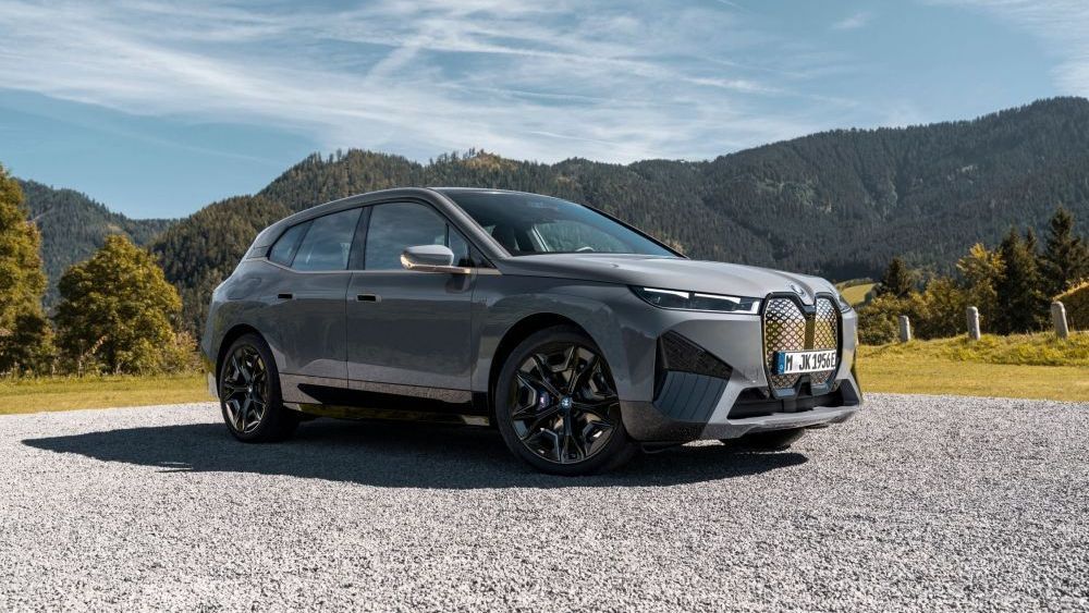 Een BMW iX M60 staat op grind met bergen op de achtergrond