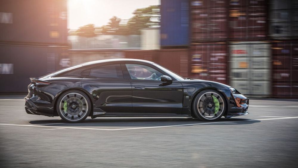 Zijkant van de Porsche Taycan getuned door Brabus rijdt op locatie in de buurt van zeecontainers