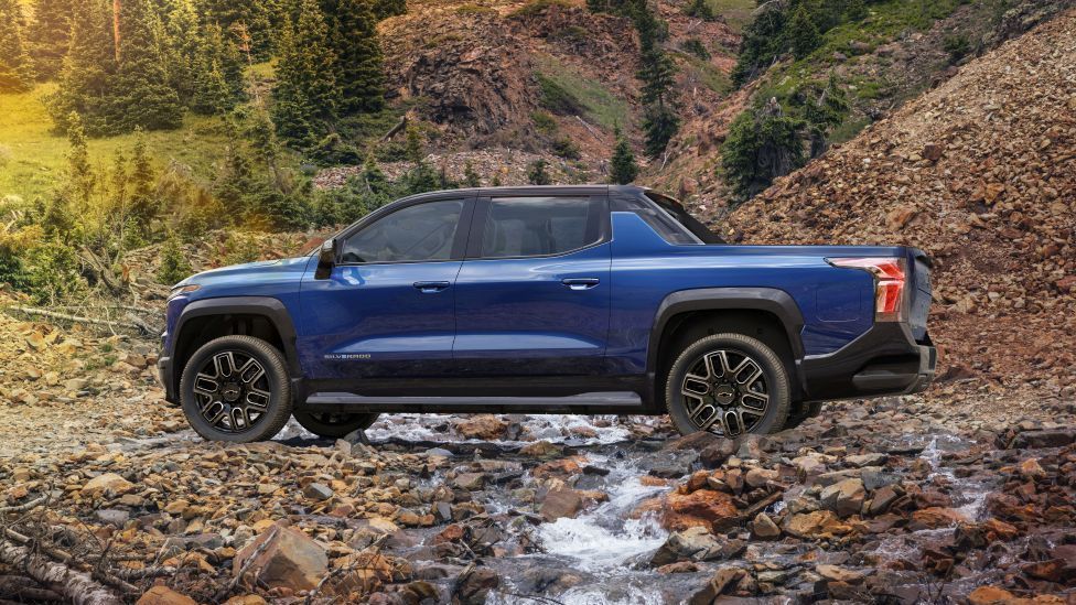 Een blauwe elektrische Silverado rijdt door een geul van keien en water
