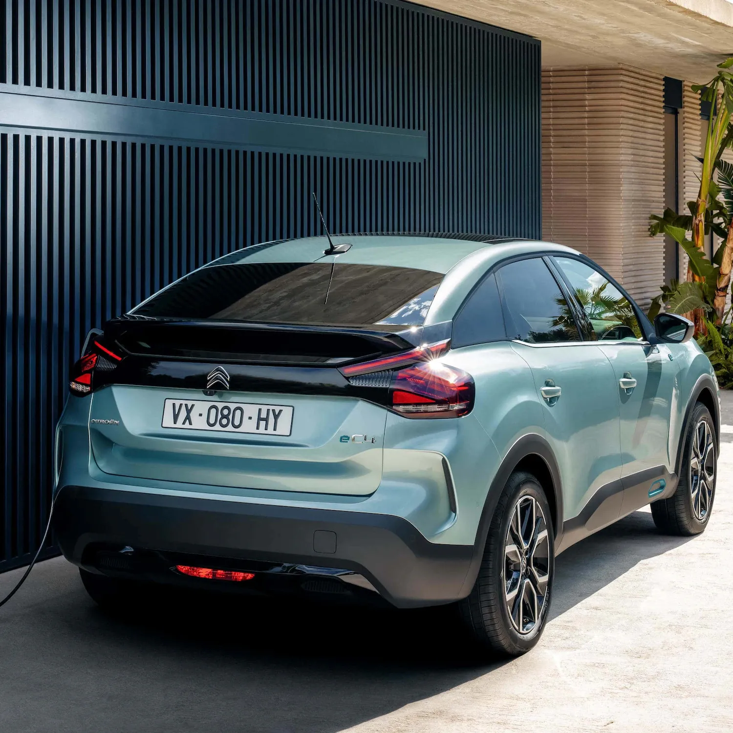 Een groene Citroën ë-C4 staat bij een gebouw geparkeerd
