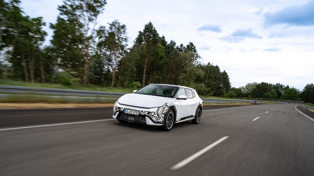 Een witte KIA EV4 rijdt over een snelweg met bomen op de achtergrond