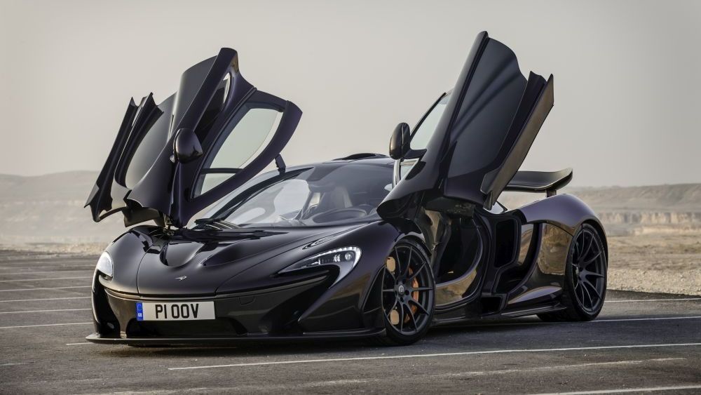 Een zwarte Mc Laren P1 staat met open deuren staat langs de kant van de weg.