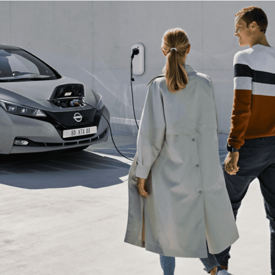 Een man en een vrouw lopen naar een elektrische auto die wordt geladen