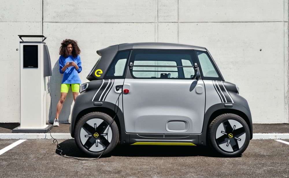 Een vrouw staat naast een Opel Rocks-e brommobiel die wordt opgeladen.