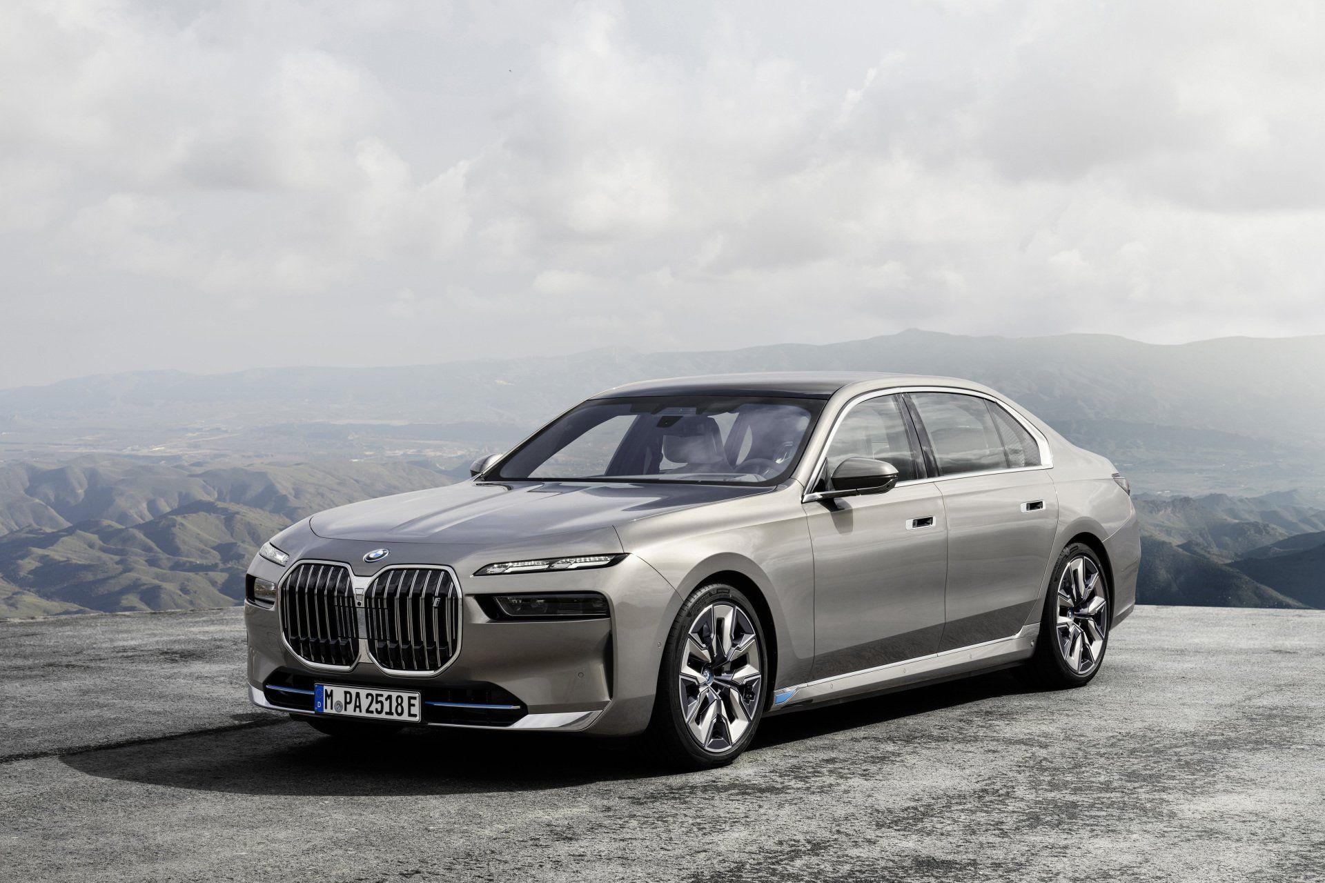 Een zilverenkleurige BMW 7-serie staat geparkeerd op een plateau aan de rand van een berg