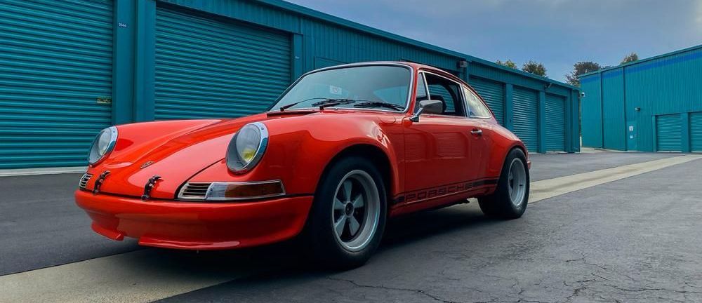 Een rode Porsche 911 ST staat voor een  gebouw met blauwe garageboxen