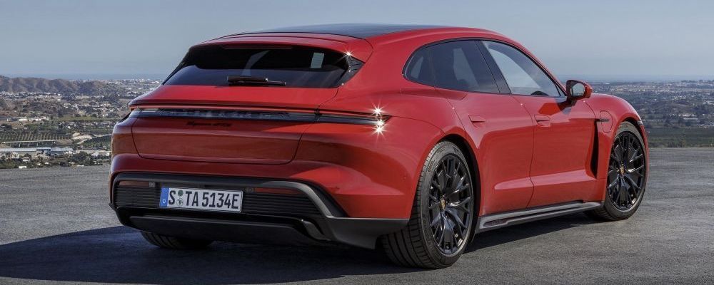 Een rode Porsche Taycan Sport Turismo staat op een hoog plateau met uitzicht