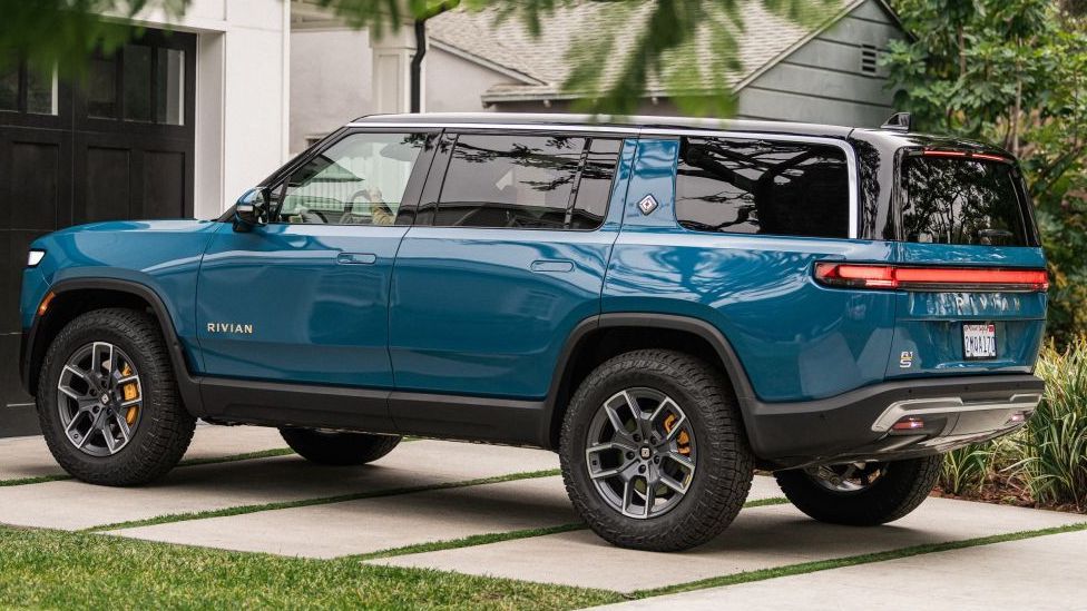 Een blauwe Rivian R1S staat op een oprit bij een woning