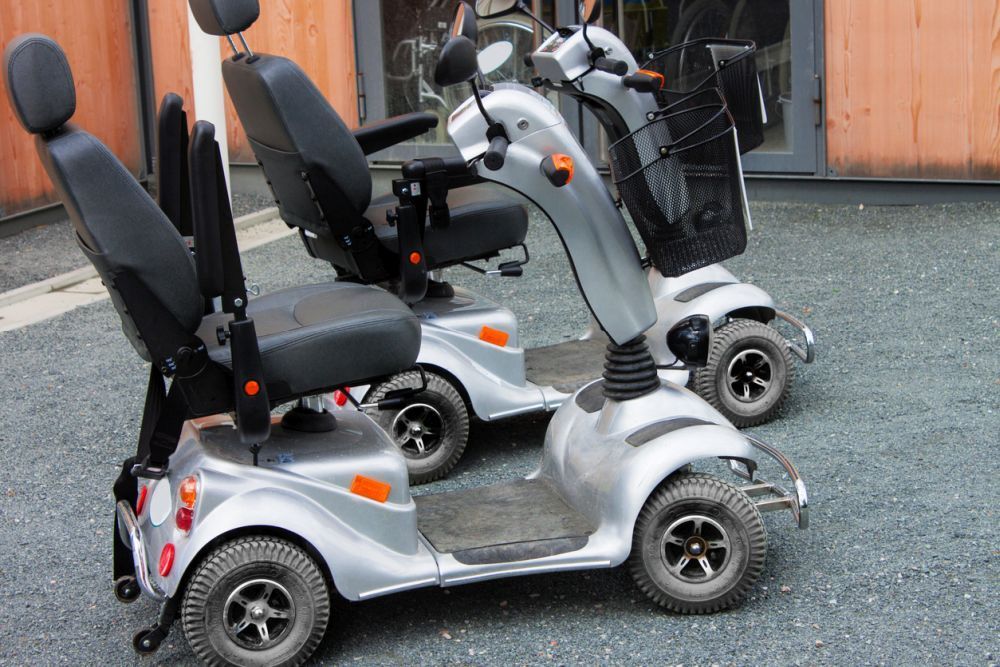 Twee gelijke scootmobielen staan bij een pand op een ondergrond van zwart grind