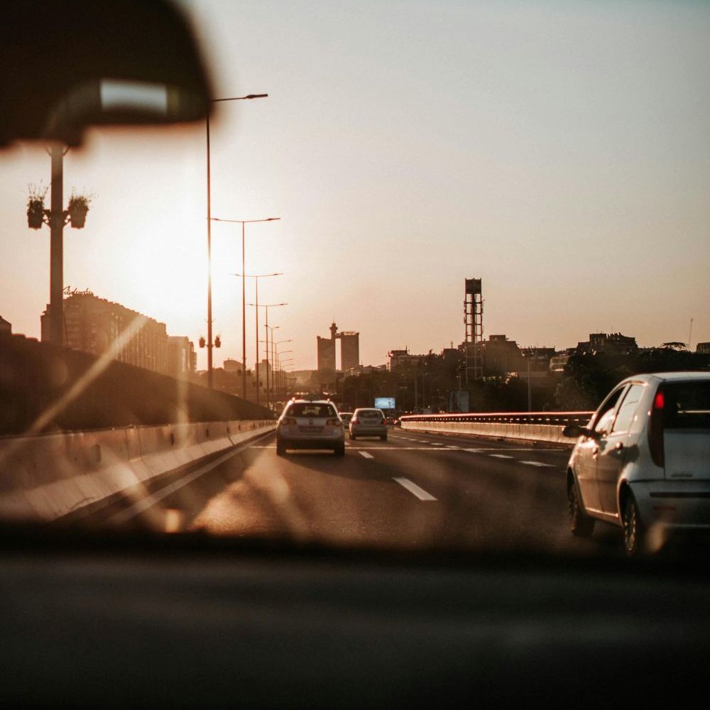 Een aantal auto's rijden over een snelweg richting de stad met ondergaande zon op de achtergrond