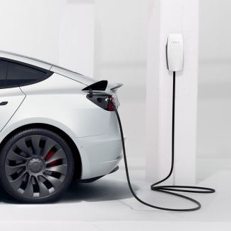 Een witte Tesla Model 3 staat aan een wallbox en wordt geladen