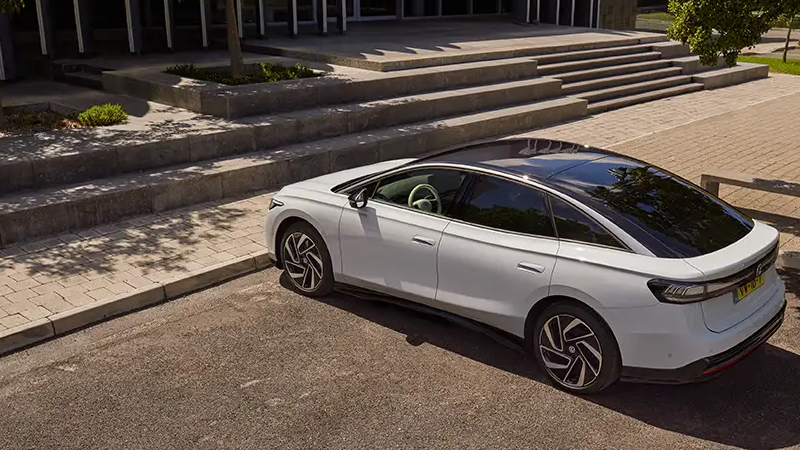 Een witte Volkswagen ID.7 staat voor een brede trap bij de ingang van een gebouw