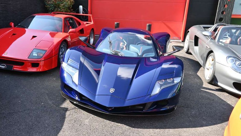 Een groep sportwagens waaronder een blauwe Aspark Owl staat bij elkaar