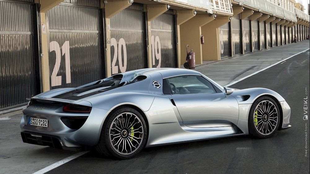 Een zilverkleurige Porsche 918 spyder staat geparkeerd voor een groot pakhuis