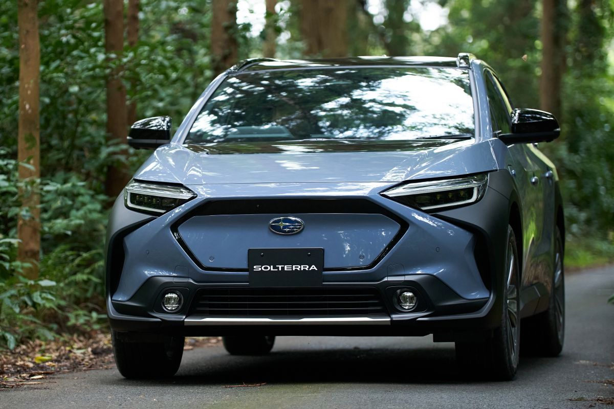 Een blauwe Subaru Solterra rijdt op een weg in het bos