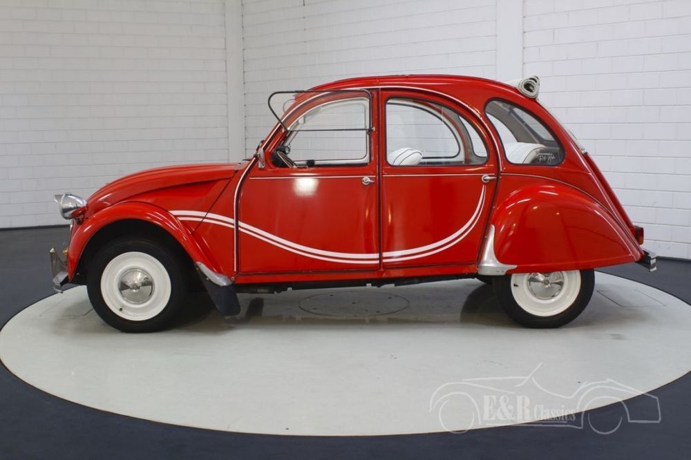 Een rode 2CV staat in een showroom met zijaanzicht