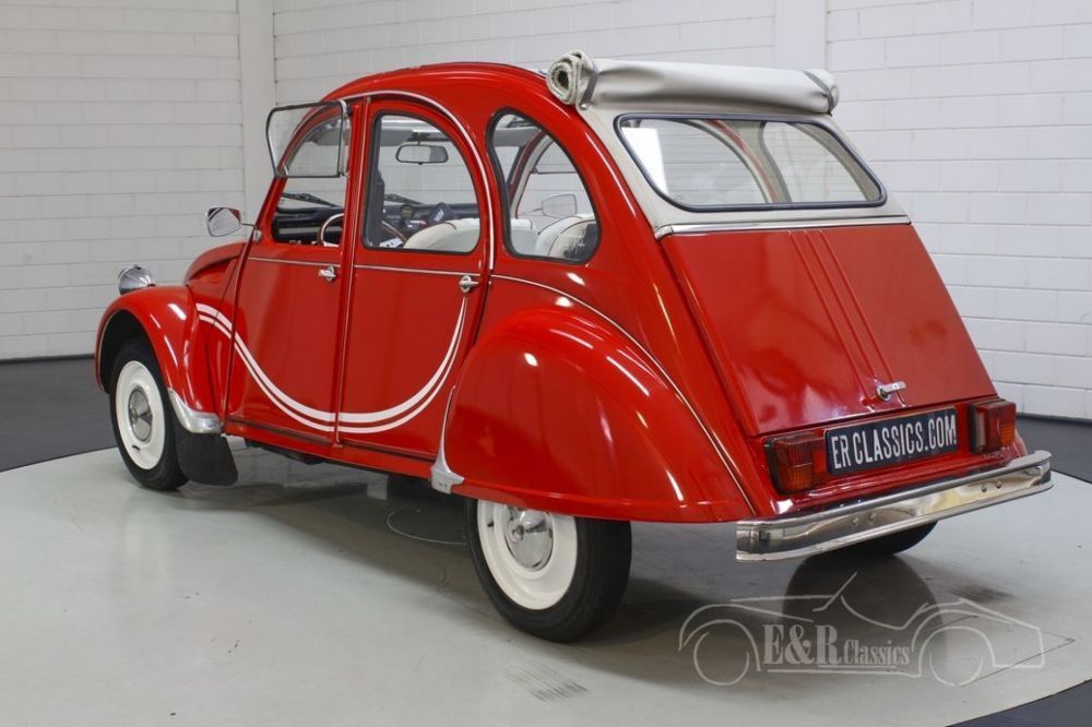 Een rode 2CV staat in een showroom vanaf links naar achteren