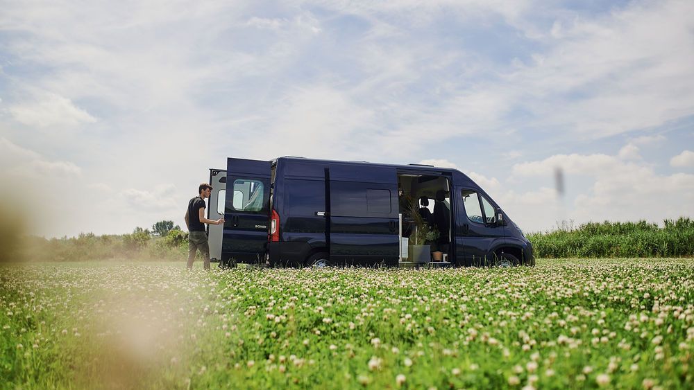 Een donkerblauwe e-camper VAN-Jorn staat in een weiland