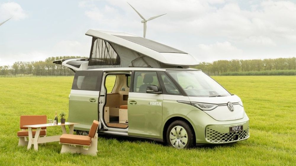 Een groene camperbus eVentje staat uitgestald in een weiland met windmolen op de achtergrond