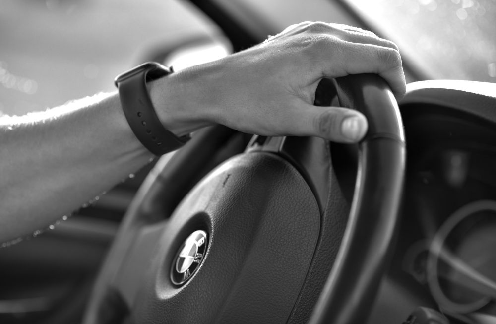 iemand met horloge draait met linkerhand aan het stuur van een auto