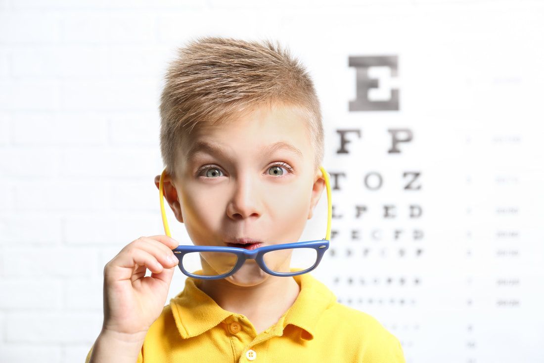 young boy in a yellow shirt and glasses in front of an eye test chart