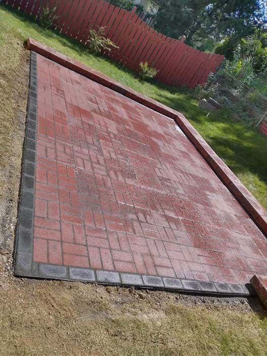 A red brick patio with a black border is being built in a backyard.