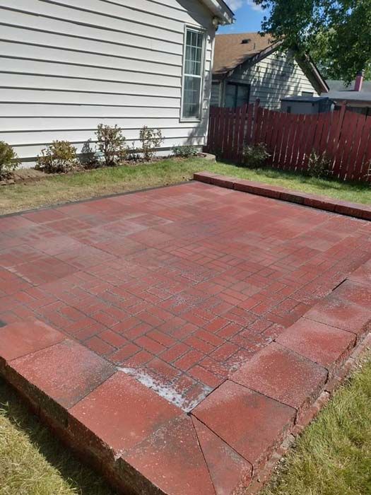 A red brick patio in the backyard of a house.