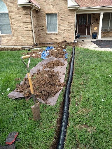 A drain pipe is being installed in the grass in front of a brick house.