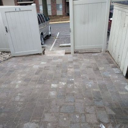 A brick walkway with a white fence and a van parked in the background.
