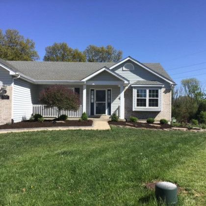 A white house with a gray roof and a large lawn in front of it.