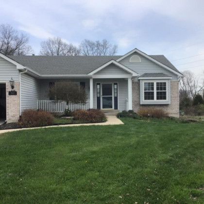 A white house with a gray roof and a large lawn in front of it.