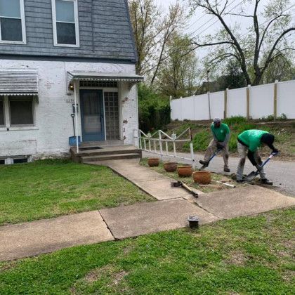 Two men are working on the sidewalk in front of a house.