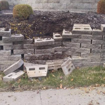 A brick wall has been damaged by a storm and is sitting on the side of the road.