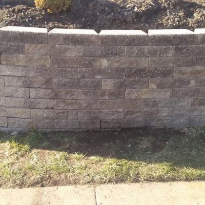 A brick wall is sitting on the side of the road next to a sidewalk.