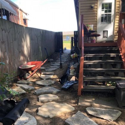 A stone walkway leading to a house with stairs and a wheelbarrow.