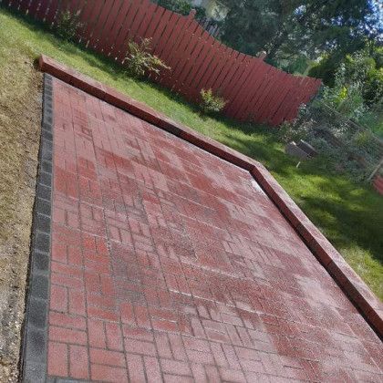 A brick walkway in a backyard with a red fence in the background.