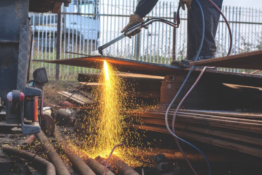 A Man Is Cutting A Piece Of Metal With A Torch — Tinman's Welding Worx In Moranbah, QLD