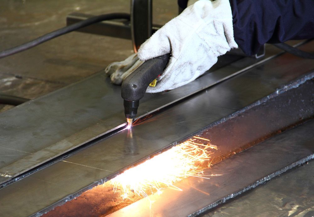 A Person Is Cutting A Piece Of Metal With A Torch — Tinman's Welding Worx In Sarina, QLD