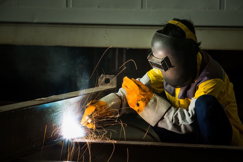 A Man Is Welding A Piece Of Metal In A Dark Room — Tinman's Welding Worx In Nebo, QLD