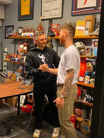 Two men are shaking hands in a room filled with lots of memorabilia.