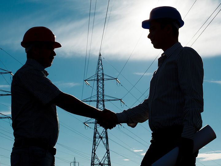 Dos hombres se dan la mano frente a cables eléctricos